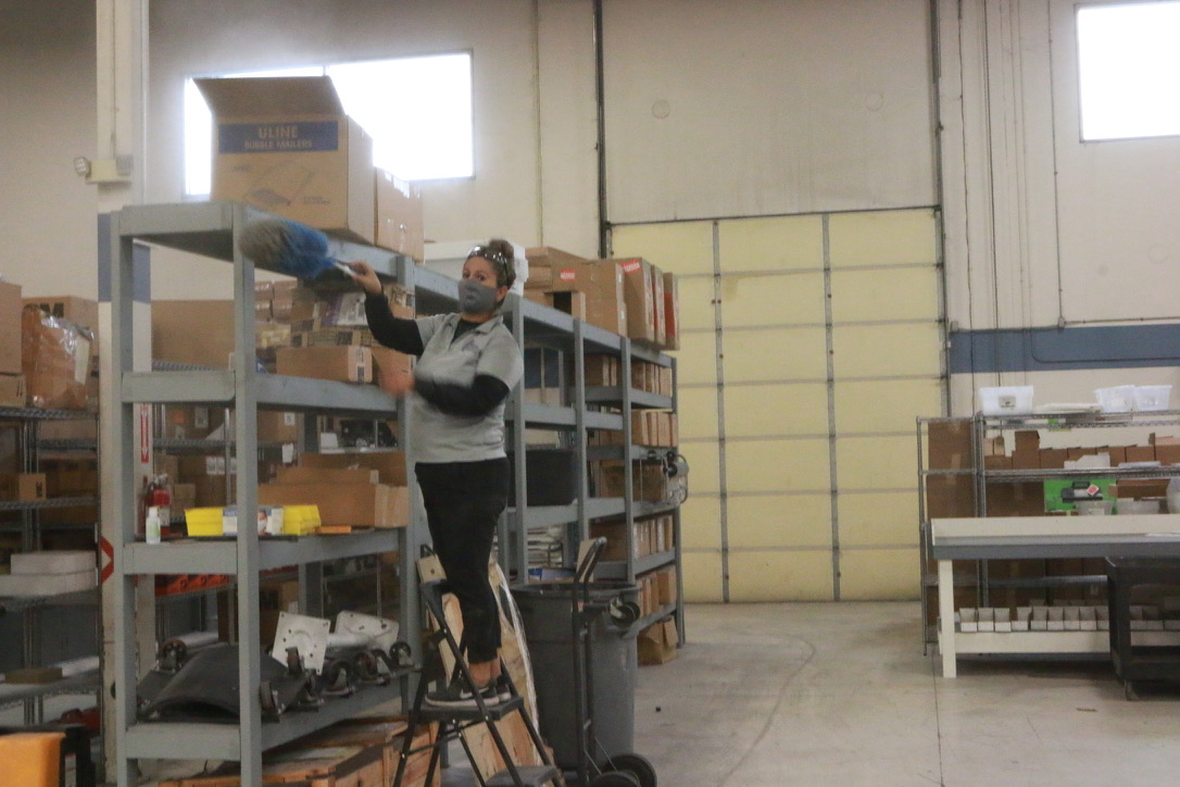 Bel Cleaning crew member high dusting warehouse storage shelves from a step ladder