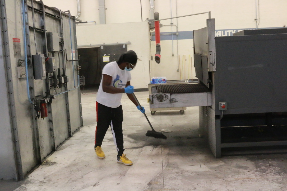 Bel Cleaning technician sweeping dust and debris on a manufacturing plant floor